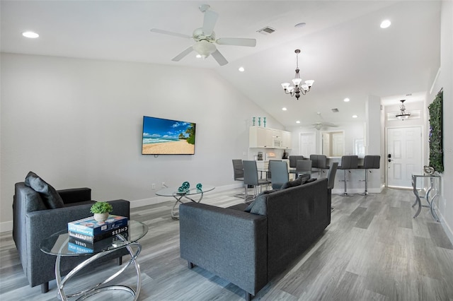 living area featuring ceiling fan with notable chandelier, light wood finished floors, lofted ceiling, and visible vents