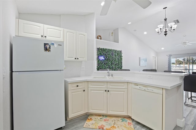 kitchen with a sink, white appliances, a peninsula, ceiling fan with notable chandelier, and light wood-style flooring