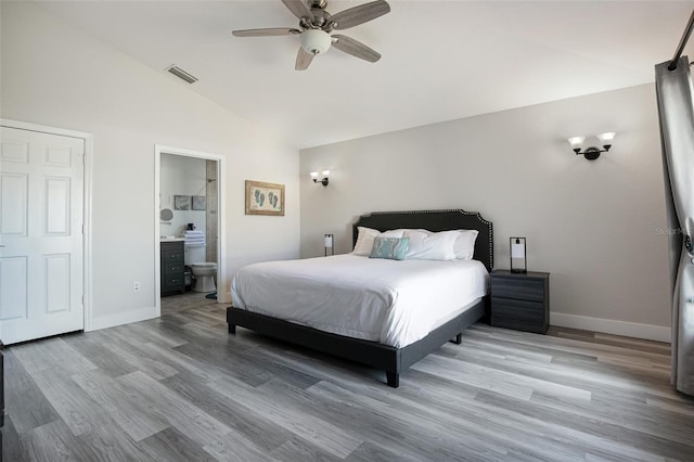 bedroom with connected bathroom, vaulted ceiling, wood finished floors, and baseboards