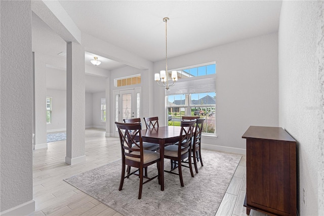 dining area with light wood-type flooring, a notable chandelier, and plenty of natural light