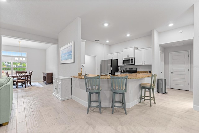 kitchen with a kitchen bar, stainless steel appliances, an inviting chandelier, white cabinetry, and light wood-type flooring