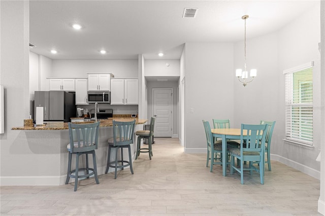 kitchen featuring white cabinets, kitchen peninsula, light hardwood / wood-style flooring, stone countertops, and appliances with stainless steel finishes