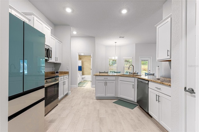 kitchen featuring sink, appliances with stainless steel finishes, a textured ceiling, hanging light fixtures, and white cabinets