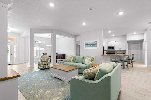 living room featuring light hardwood / wood-style floors, a textured ceiling, and a notable chandelier