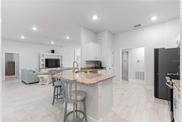 kitchen featuring sink, a breakfast bar, light stone countertops, white cabinetry, and light wood-type flooring