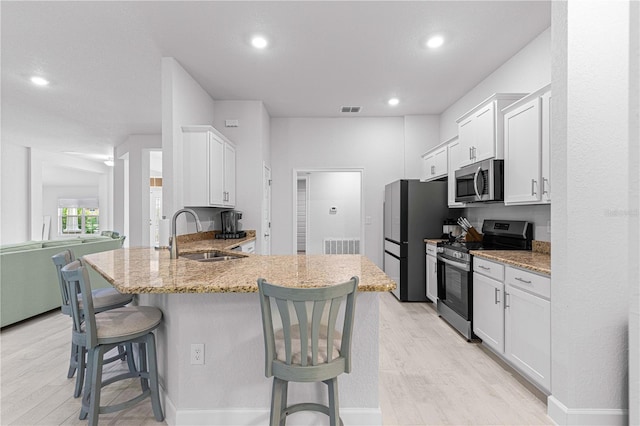 kitchen featuring stainless steel appliances, white cabinets, kitchen peninsula, sink, and a breakfast bar