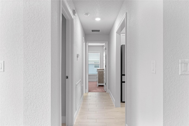 hallway with a textured ceiling and light wood-type flooring