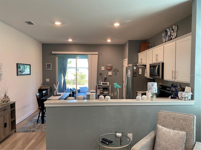 kitchen with white cabinets, light wood-type flooring, black appliances, and kitchen peninsula