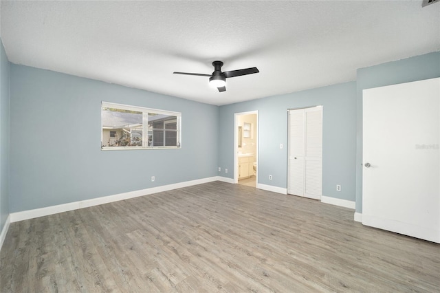 unfurnished bedroom with ceiling fan, ensuite bath, light wood-type flooring, a closet, and a textured ceiling