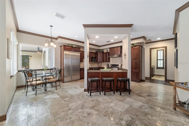 kitchen with appliances with stainless steel finishes, tasteful backsplash, wall chimney exhaust hood, decorative light fixtures, and a notable chandelier