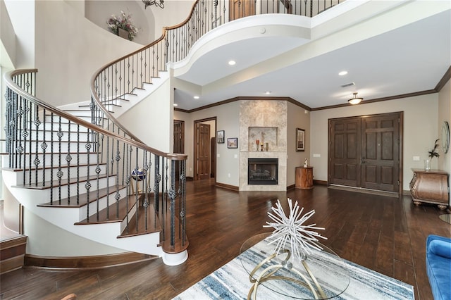 entryway featuring a tile fireplace, hardwood / wood-style floors, a towering ceiling, and ornamental molding