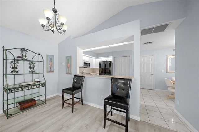 kitchen featuring black refrigerator, kitchen peninsula, light wood-type flooring, vaulted ceiling, and white cabinetry