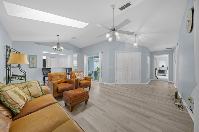 living room featuring vaulted ceiling with skylight, ceiling fan with notable chandelier, and light wood-type flooring