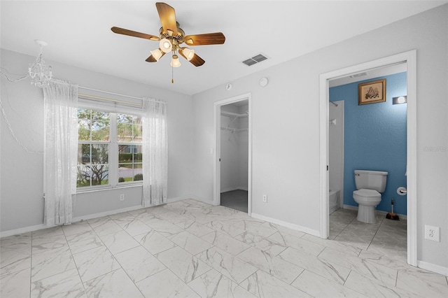 unfurnished bedroom with ceiling fan with notable chandelier, a closet, a spacious closet, and ensuite bath