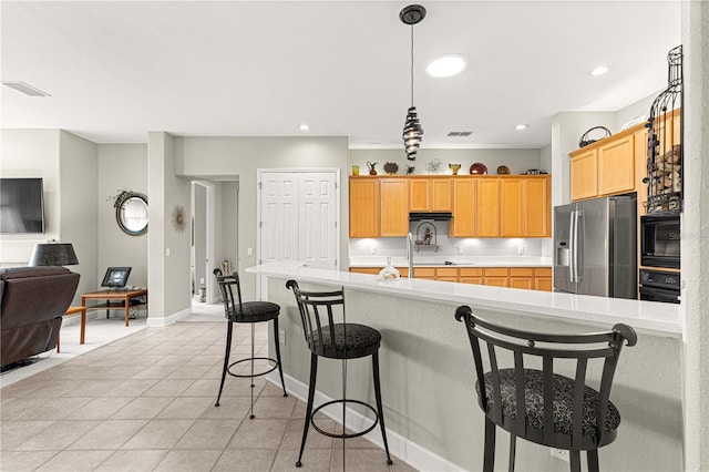 kitchen with stainless steel refrigerator with ice dispenser, a breakfast bar area, light tile patterned floors, black microwave, and pendant lighting