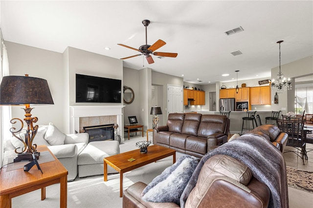 living room featuring a tiled fireplace, light carpet, and ceiling fan with notable chandelier