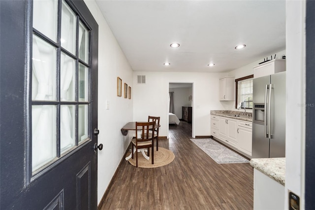 kitchen featuring dark wood-type flooring, white cabinets, stainless steel refrigerator with ice dispenser, sink, and light stone countertops