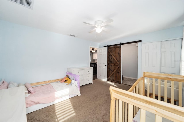 carpeted bedroom with a barn door, ceiling fan, and a closet