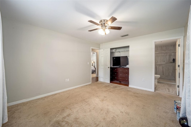 unfurnished bedroom with a closet, light colored carpet, ensuite bath, and ceiling fan