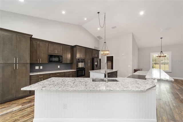 kitchen with sink, black appliances, hardwood / wood-style floors, a spacious island, and vaulted ceiling