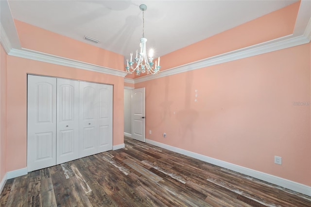 unfurnished bedroom with dark hardwood / wood-style flooring, a closet, a notable chandelier, and crown molding