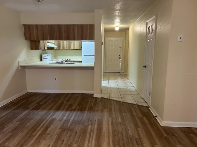 kitchen featuring sink, dark wood-type flooring, kitchen peninsula, white fridge, and range