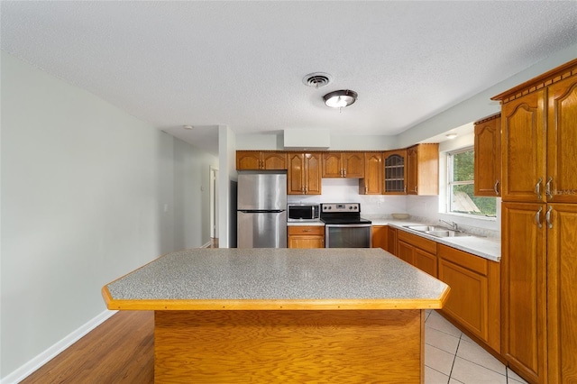 kitchen featuring a center island, sink, light tile patterned floors, a textured ceiling, and appliances with stainless steel finishes