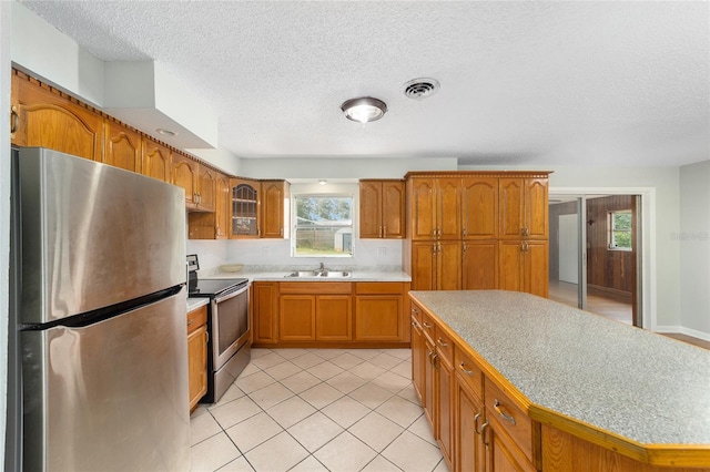 kitchen featuring a textured ceiling, stainless steel appliances, sink, a center island, and light tile patterned flooring