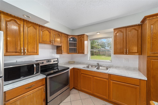 kitchen with decorative backsplash, a textured ceiling, stainless steel appliances, sink, and light tile patterned floors