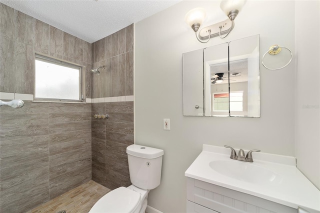 bathroom featuring ceiling fan, a textured ceiling, tiled shower, toilet, and vanity