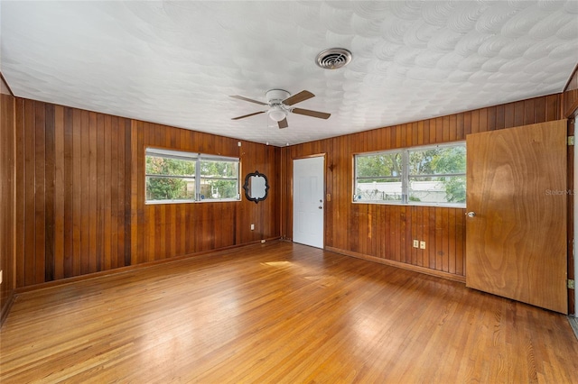 unfurnished room featuring wood walls, ceiling fan, a healthy amount of sunlight, and light hardwood / wood-style flooring