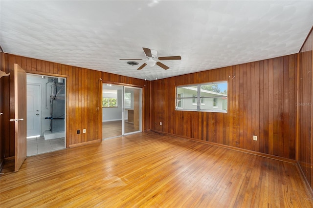 empty room with ceiling fan, wood walls, and light hardwood / wood-style flooring