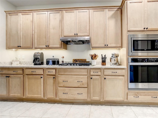 kitchen featuring light brown cabinets, stainless steel appliances, light tile patterned flooring, and light stone countertops