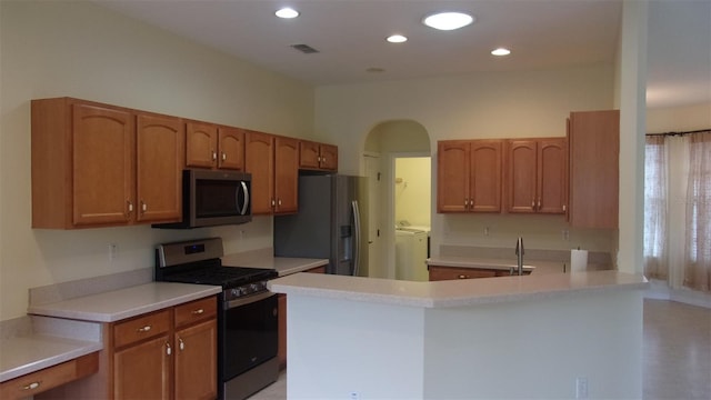 kitchen with washing machine and dryer, kitchen peninsula, sink, and stainless steel appliances