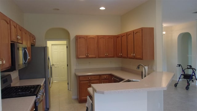 kitchen with kitchen peninsula, sink, light tile patterned floors, and stainless steel appliances