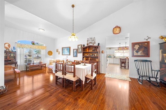 dining space featuring hardwood / wood-style flooring, high vaulted ceiling, and an inviting chandelier