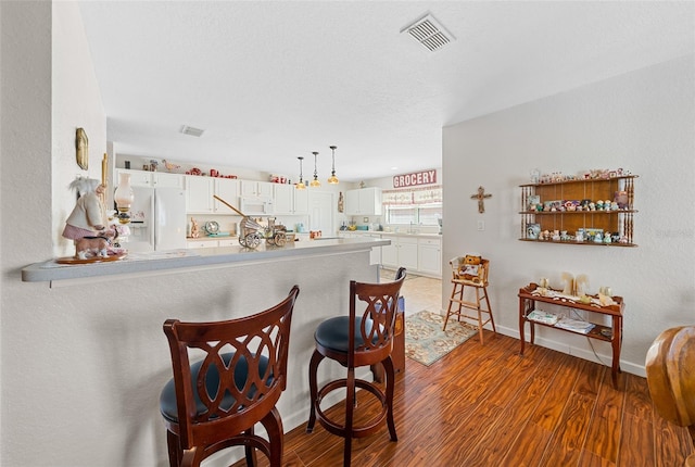 kitchen with kitchen peninsula, white appliances, dark hardwood / wood-style floors, and white cabinetry