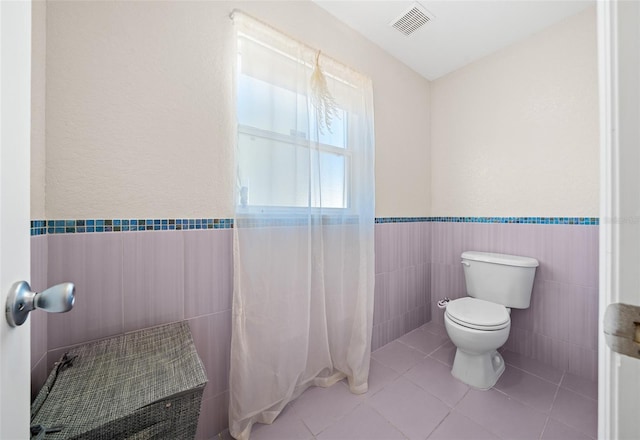 bathroom with tile patterned flooring, toilet, and tile walls