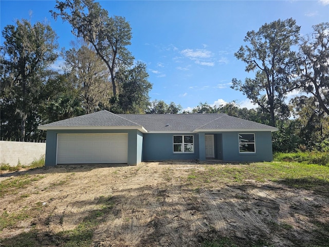 ranch-style house featuring a shingled roof, a garage, dirt driveway, and stucco siding