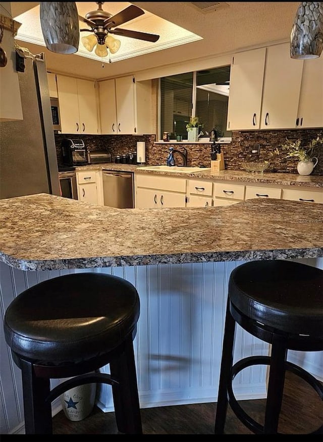 kitchen featuring white cabinetry, sink, light stone counters, a kitchen bar, and stainless steel dishwasher