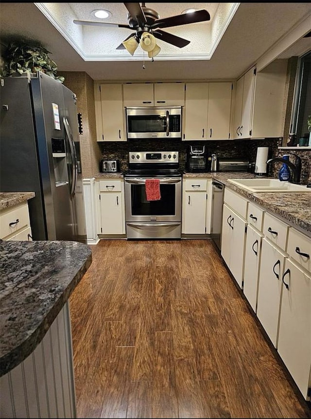 kitchen with appliances with stainless steel finishes, a raised ceiling, sink, dark wood-type flooring, and ceiling fan