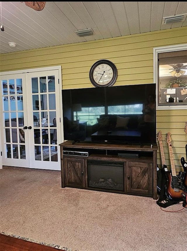 living room featuring french doors, wood walls, and carpet