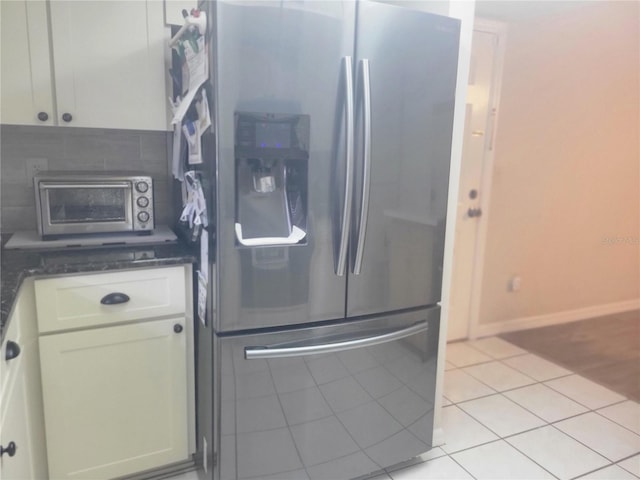 kitchen with dark stone counters, stainless steel refrigerator with ice dispenser, white cabinetry, and light tile patterned floors