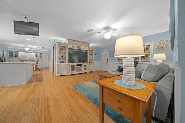 living room with a textured ceiling, light hardwood / wood-style floors, ceiling fan, and a healthy amount of sunlight