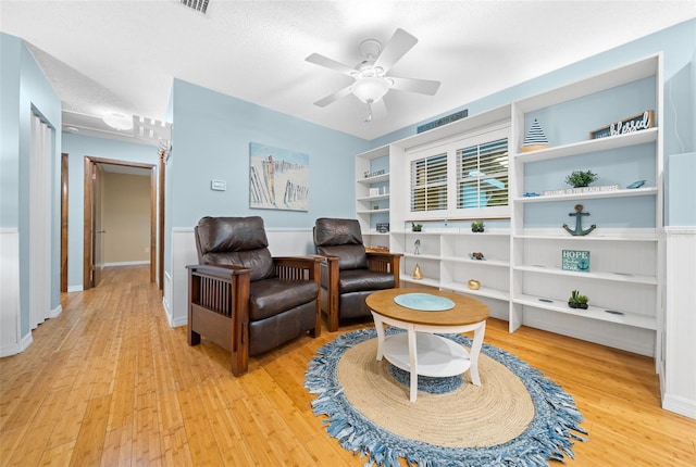 living area featuring built in shelves, ceiling fan, a textured ceiling, and light wood-type flooring