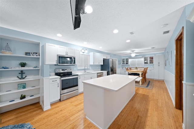 kitchen with a center island, light hardwood / wood-style floors, a textured ceiling, white cabinets, and appliances with stainless steel finishes