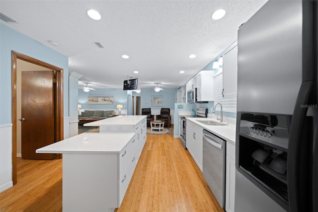 kitchen featuring white cabinets, light wood-type flooring, stainless steel appliances, and a kitchen island