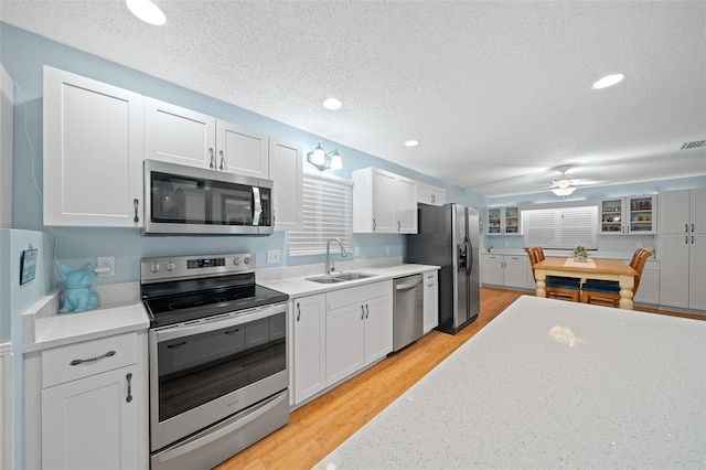 kitchen featuring sink, a textured ceiling, appliances with stainless steel finishes, light hardwood / wood-style floors, and white cabinetry