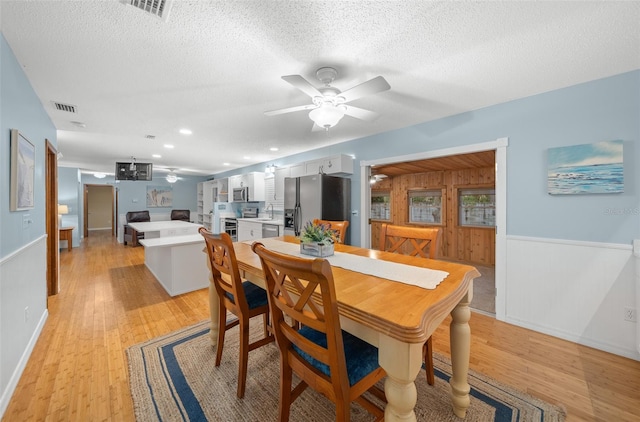 dining area with a textured ceiling, light hardwood / wood-style floors, ceiling fan, and wood walls