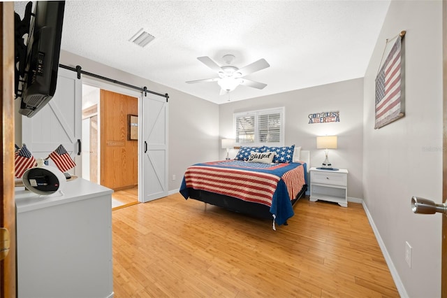 bedroom with a barn door, ceiling fan, hardwood / wood-style floors, and a textured ceiling